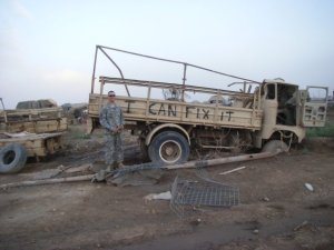 soldier in front of broken truck with sign that reads I can fix it
